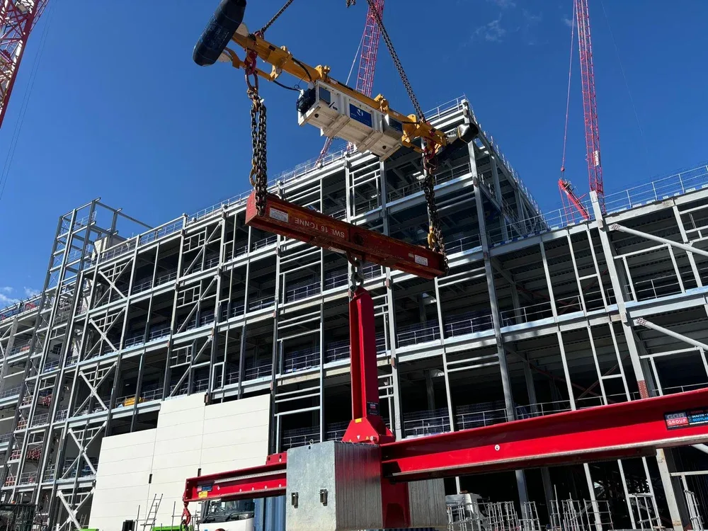 Construction site with a multi-story steel frame building, a red crane, and a blue sky.
