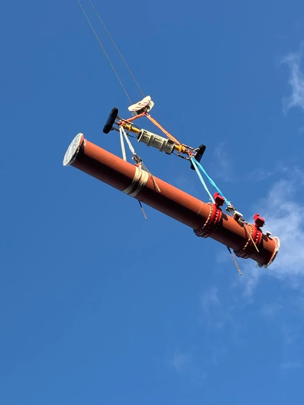A large electrical transformer or component suspended in the sky against a blue sky with a few clouds.