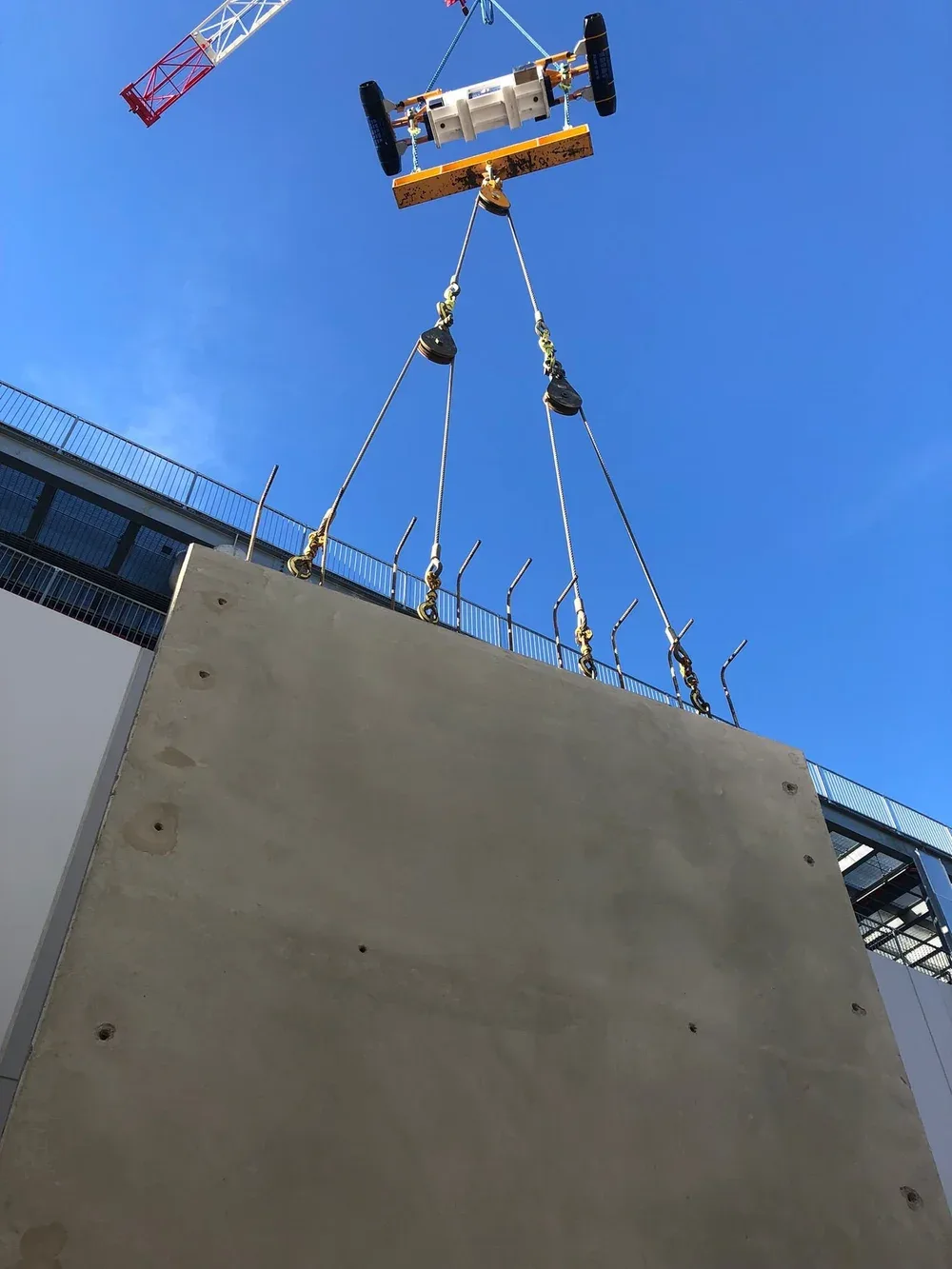 A crane lifting a large, flat concrete panel at a construction site against a blue sky background.