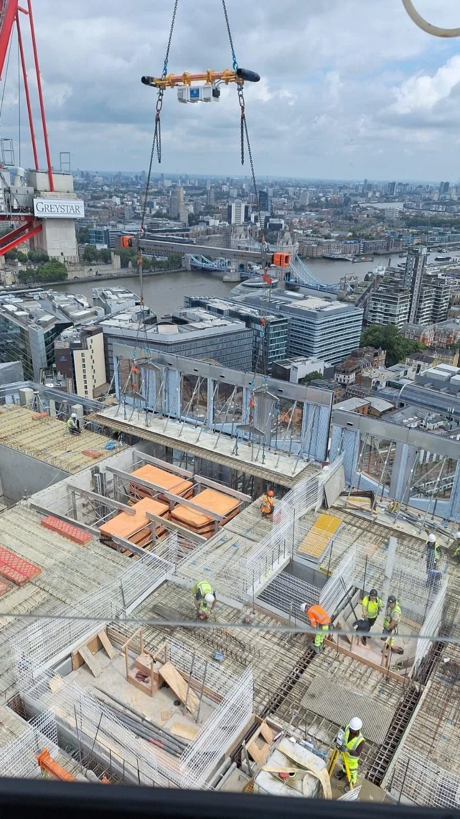 Construction workers working on a high-rise building under construction in London with the River Thames and Tower Bridge in the background.