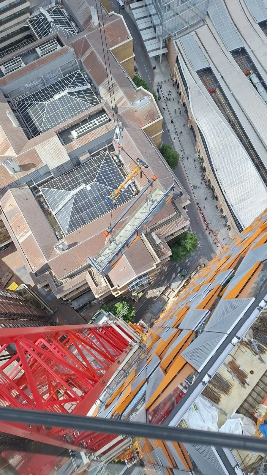 View from a high-rise building of a city street, with construction equipment and workers on a crane on the rooftop of a tall building.