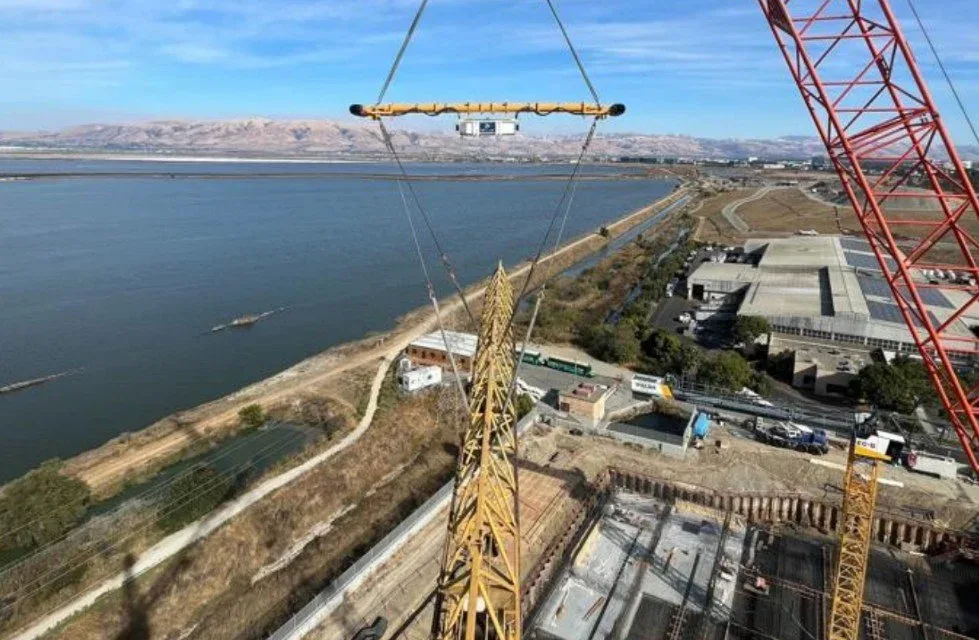 Construction site with a large yellow crane and a view of a river and mountains in the background