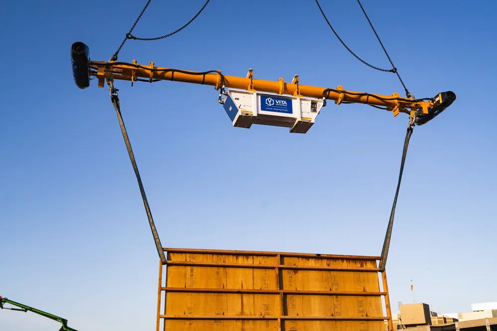 Construction crane lifting a large golden-yellow container or panel at a construction site during daytime.