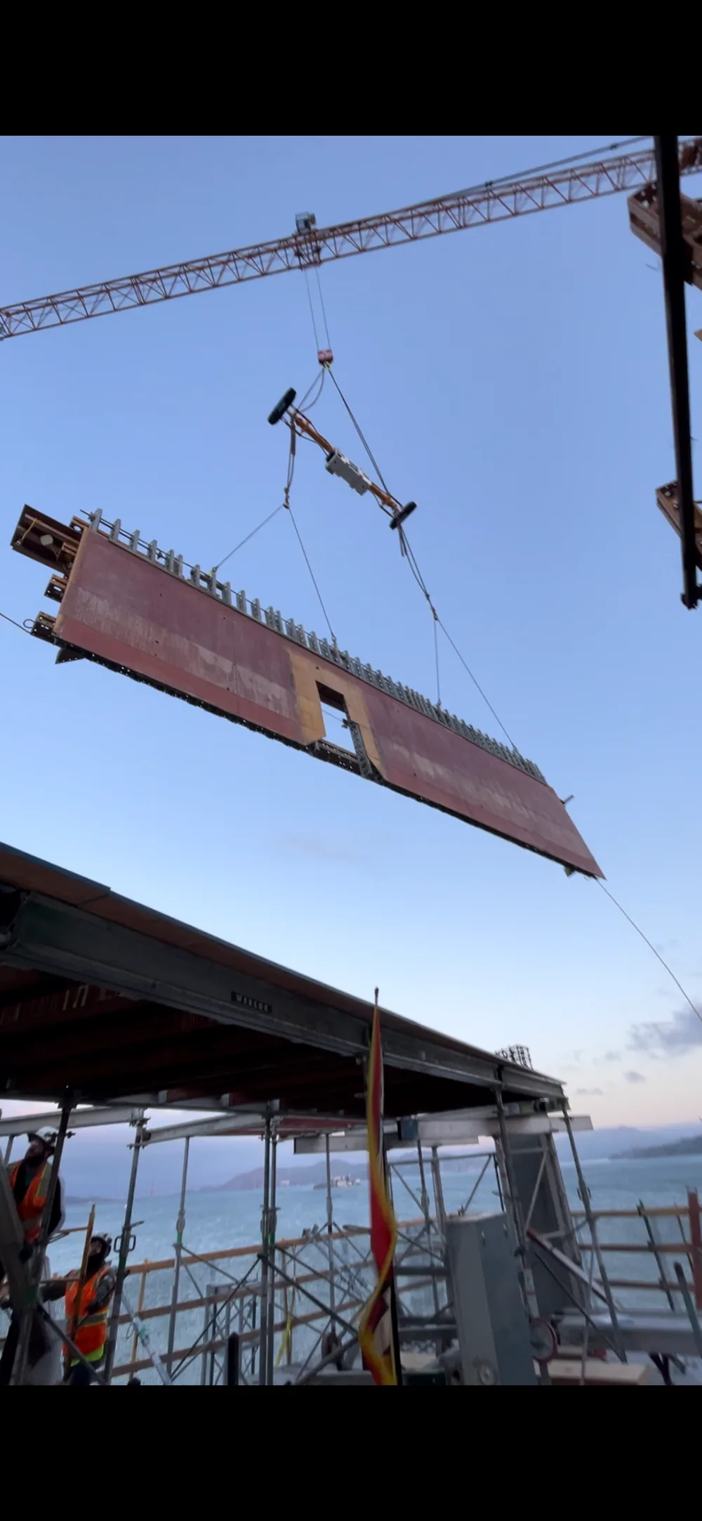 Construction workers are installing a large prefabricated building wall panel using a vln at a construction site in windy conditions
