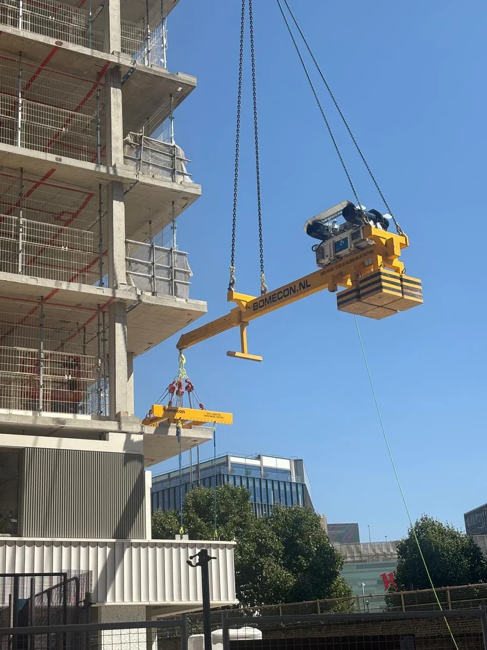 Construction site with a partially built multi-story building. A rocketlever is lifting a load into a hard to reach space. The sky is clear and blue, and there are modern glass buildings and trees in the background.