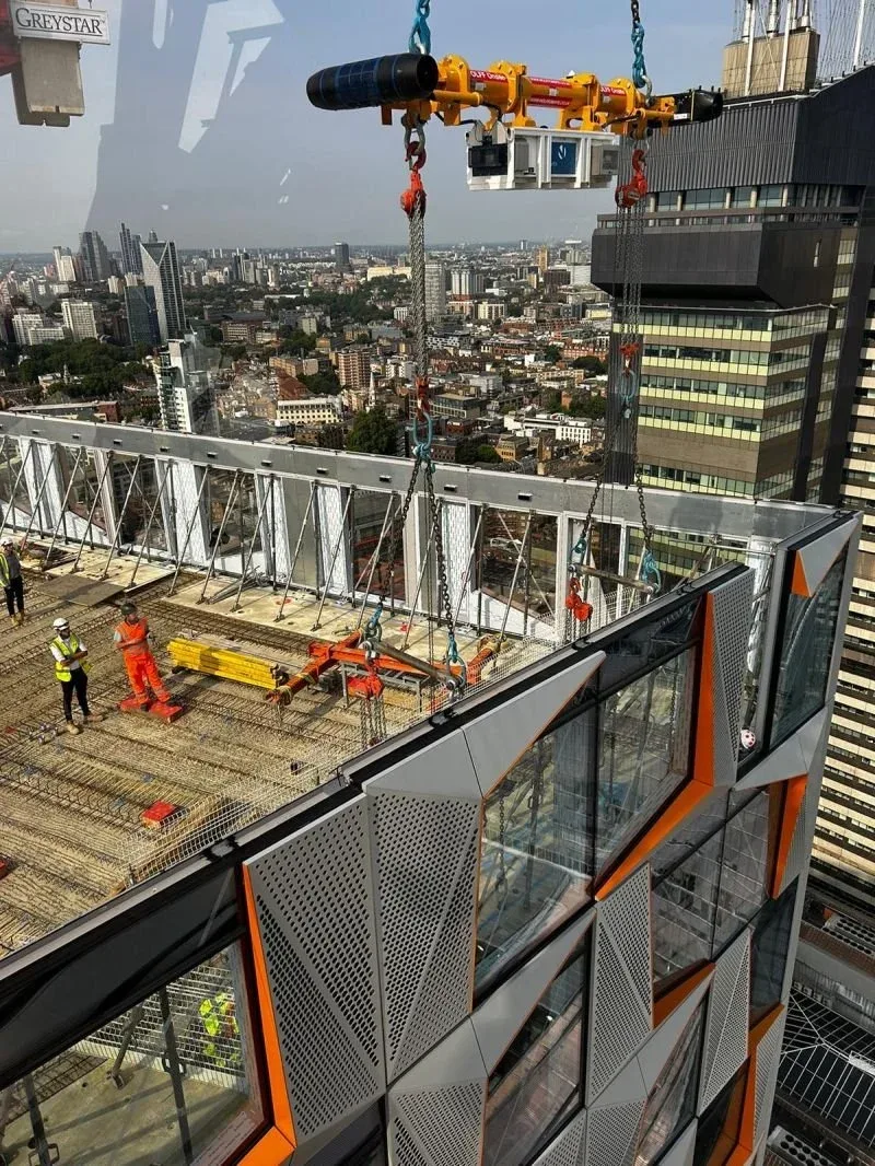 Construction workers on the rooftop of a skyscraper, installing glass panels with a safety crane, city skyline in the background.