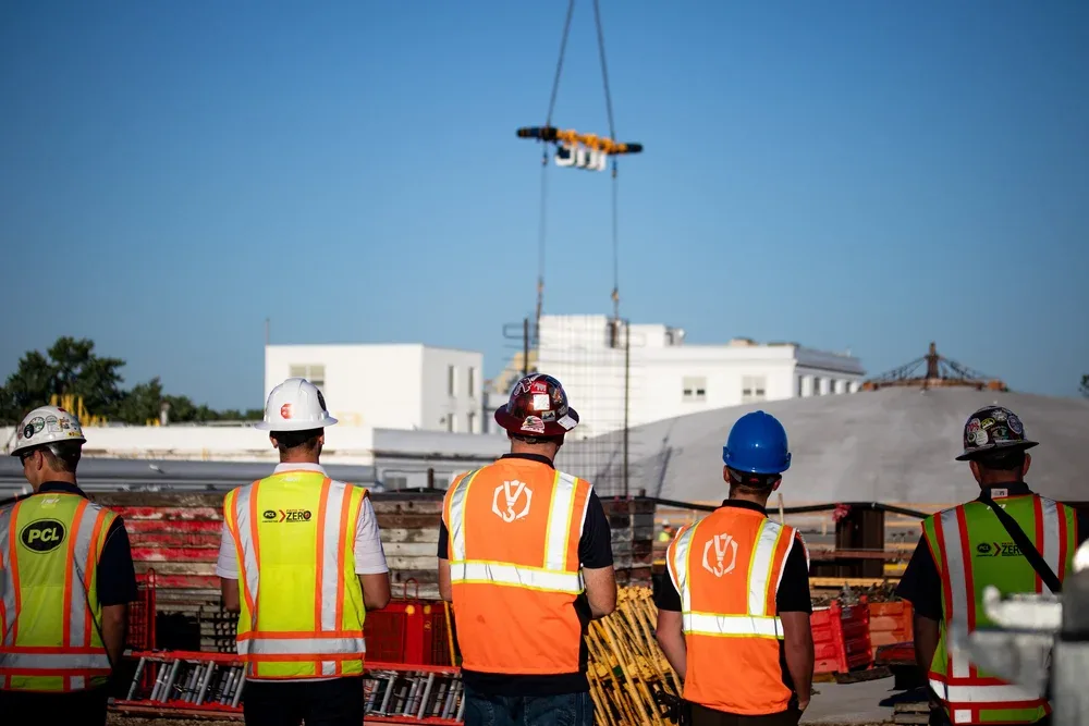 Construction workers in safety vests and helmets overseeing construction site with crane in background.