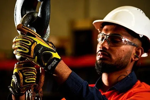 A male worker in safety glasses and a white hard hat holds a heavy-duty chain with both hands.